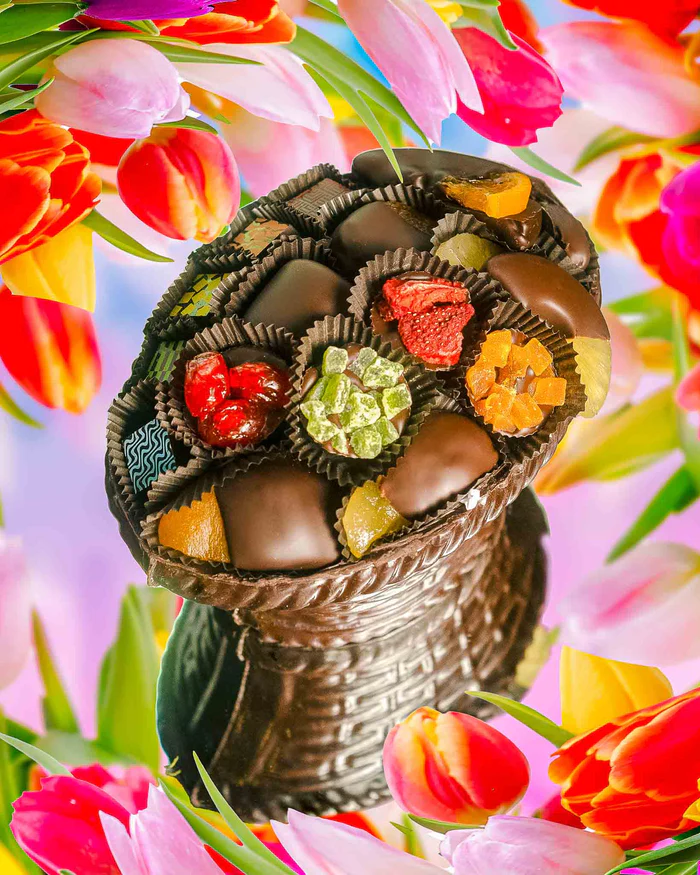 The Compartés Edible Chocolate Basket - Luxury Dark Chocolate Oval filled with various fruit clusters and truffles, on a colorful background with tulips.