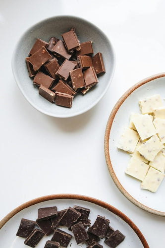 An assortment of white, dark, and milk chocolate pieces on white dishes.