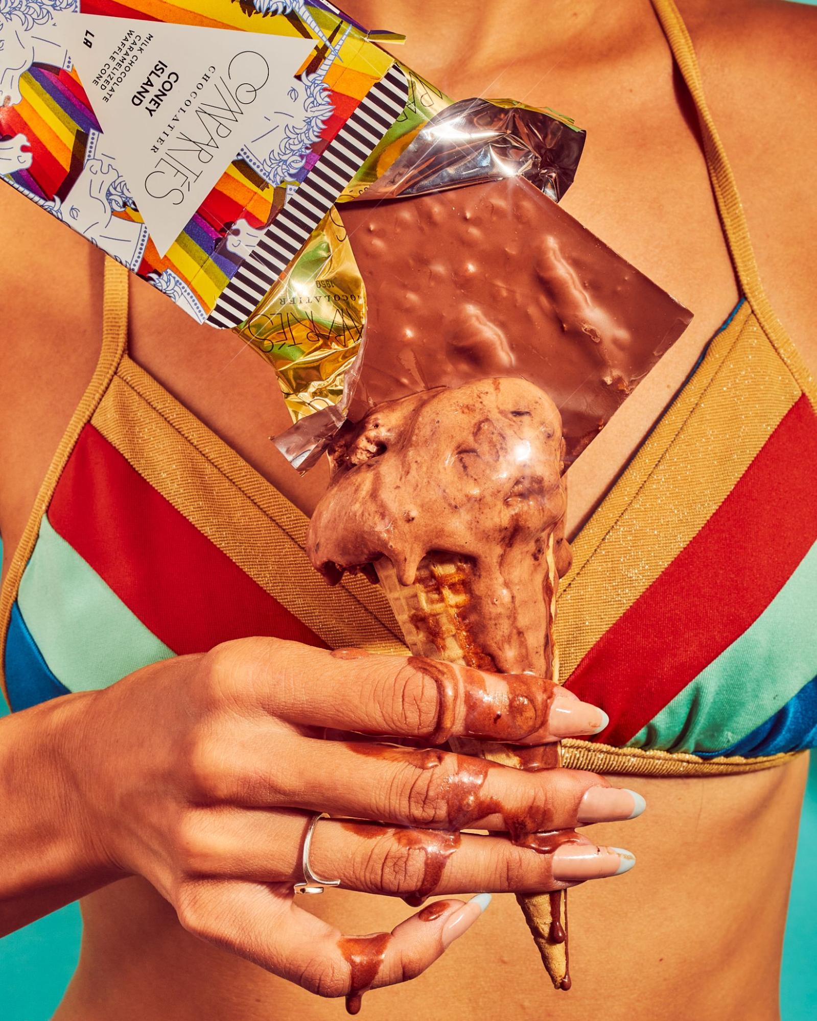 Woman in striped bikini top holding melting chocolate icecream cone with Compartés Coney Island chocolate bar on top.