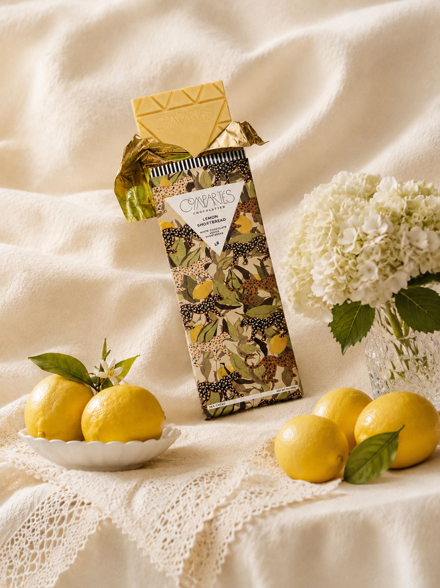 Compartes Fancy Chocolate Bar series of Lemon Shortbread with White Chocolate and Lemon on a gorgeous white tablescape with flowers and lemons.